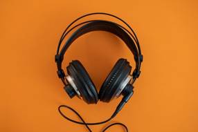 Wired headphones with cushy ear covers and overhead band. The background is orange