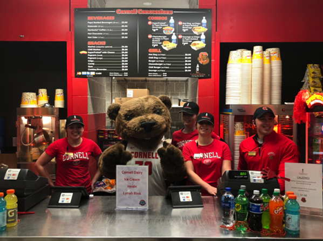 Cornell's Big Red Bear standing behind a concession stand with employees.
