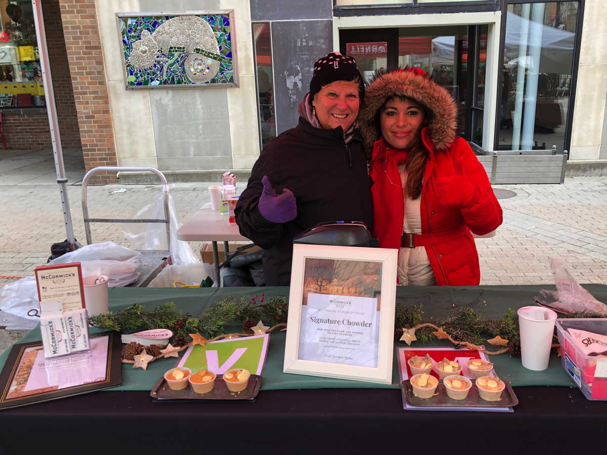 Two people bundled up in warm coats at a chowder event booth