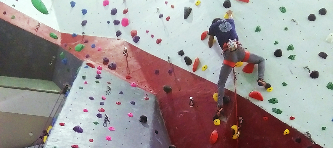 A student lead climbing high on the climbing wall