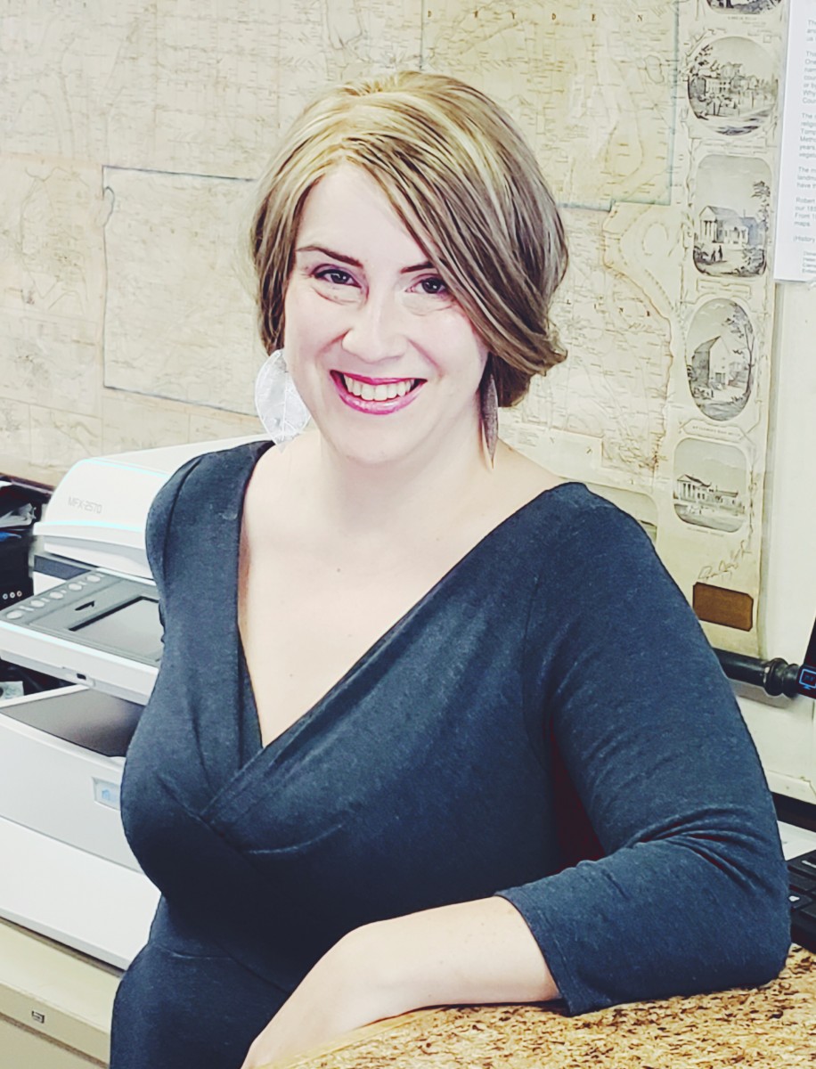 Photograph of Ellen Mary Woods leaning on a counter while smiling at the camera