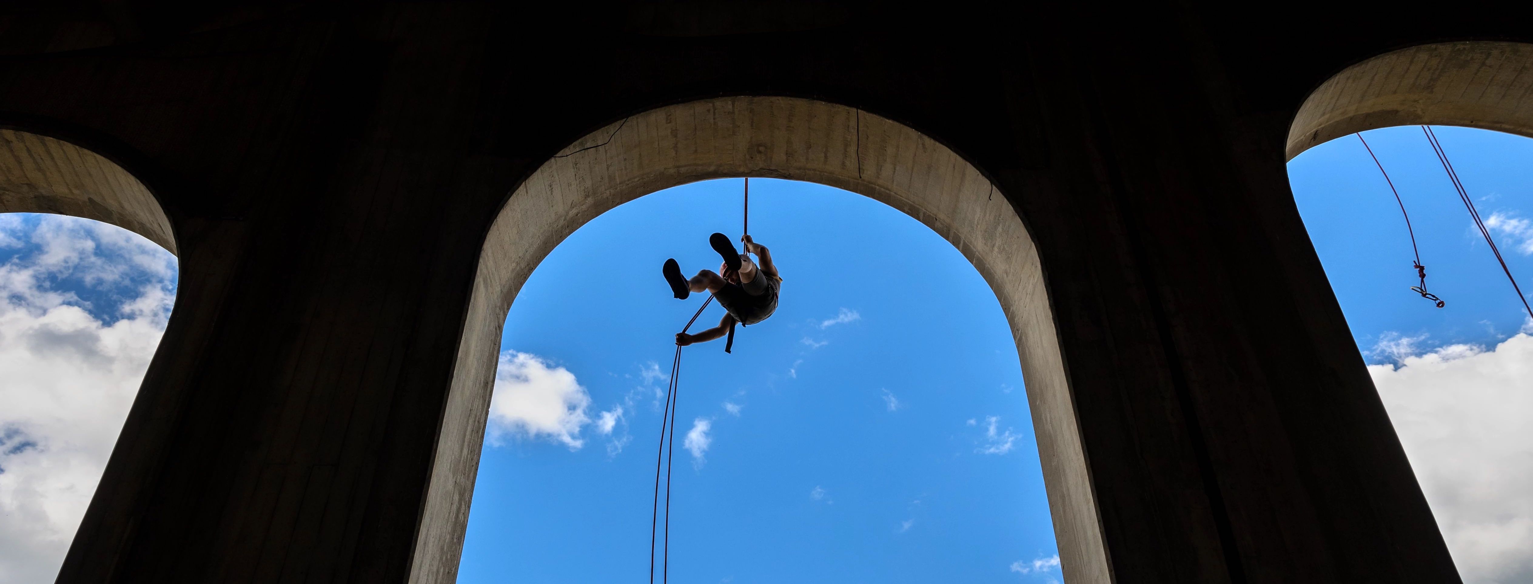 blue sky and three archways with a person rappel down a rope in the center arch off of Cornell's Schoellkopf Stadium