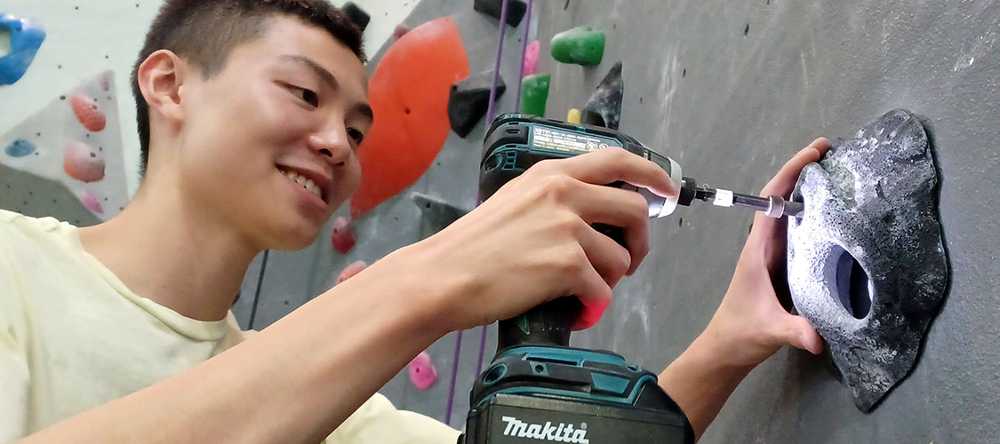 A student is attaching a climbing hold to the climbing wall.