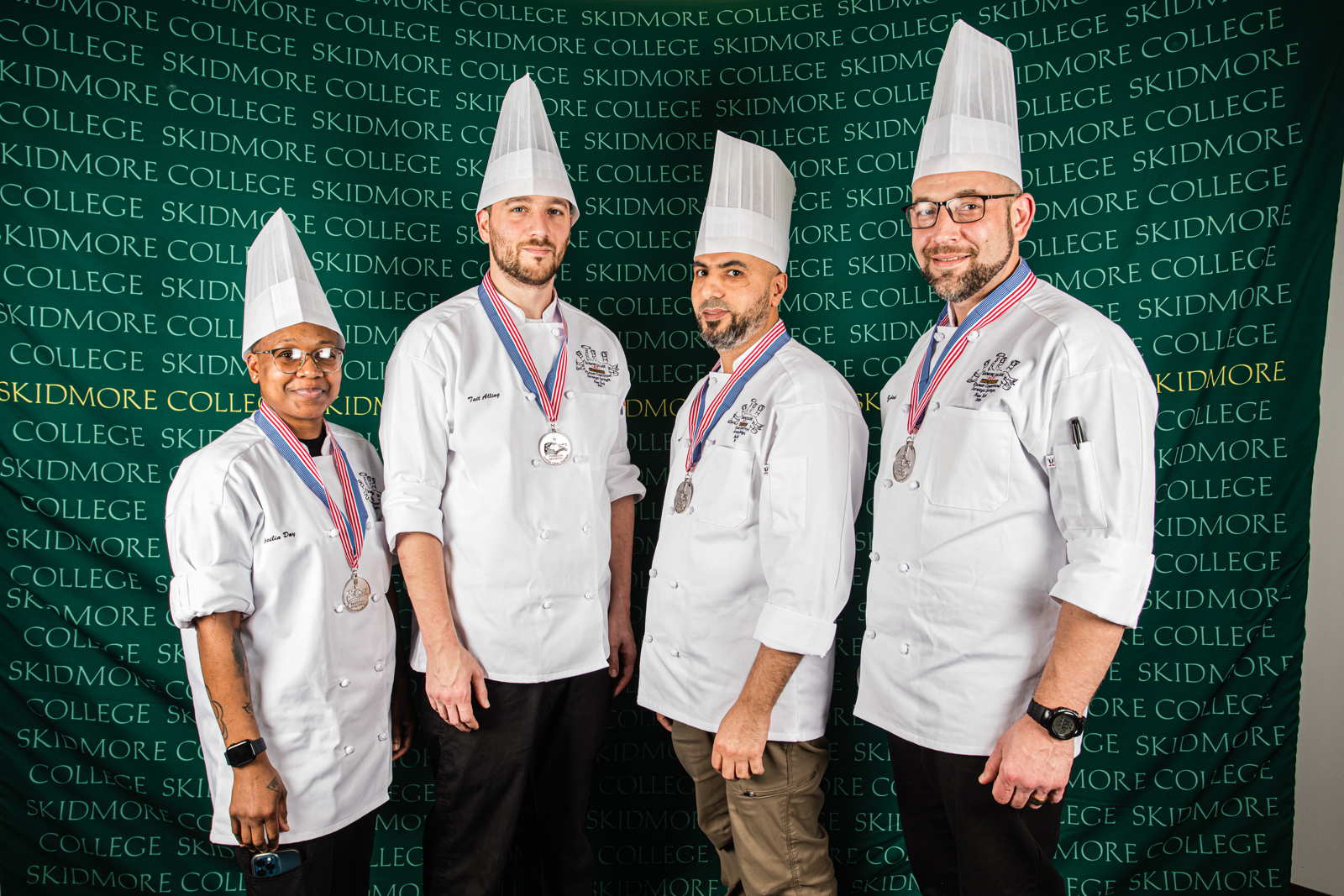 Four people in chef coats and hats wearing silver medals