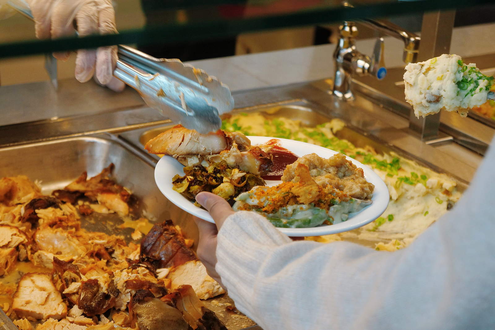 A person holds a plate of food in front of a serving line