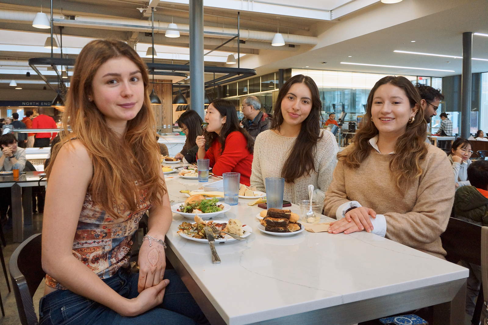 Three young women sit at a dining table with plates of food