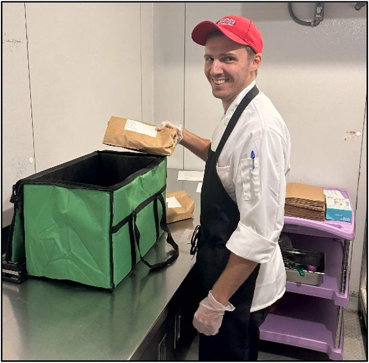 A smiling person in an apron places a paper-wrapped item in a large open cooler