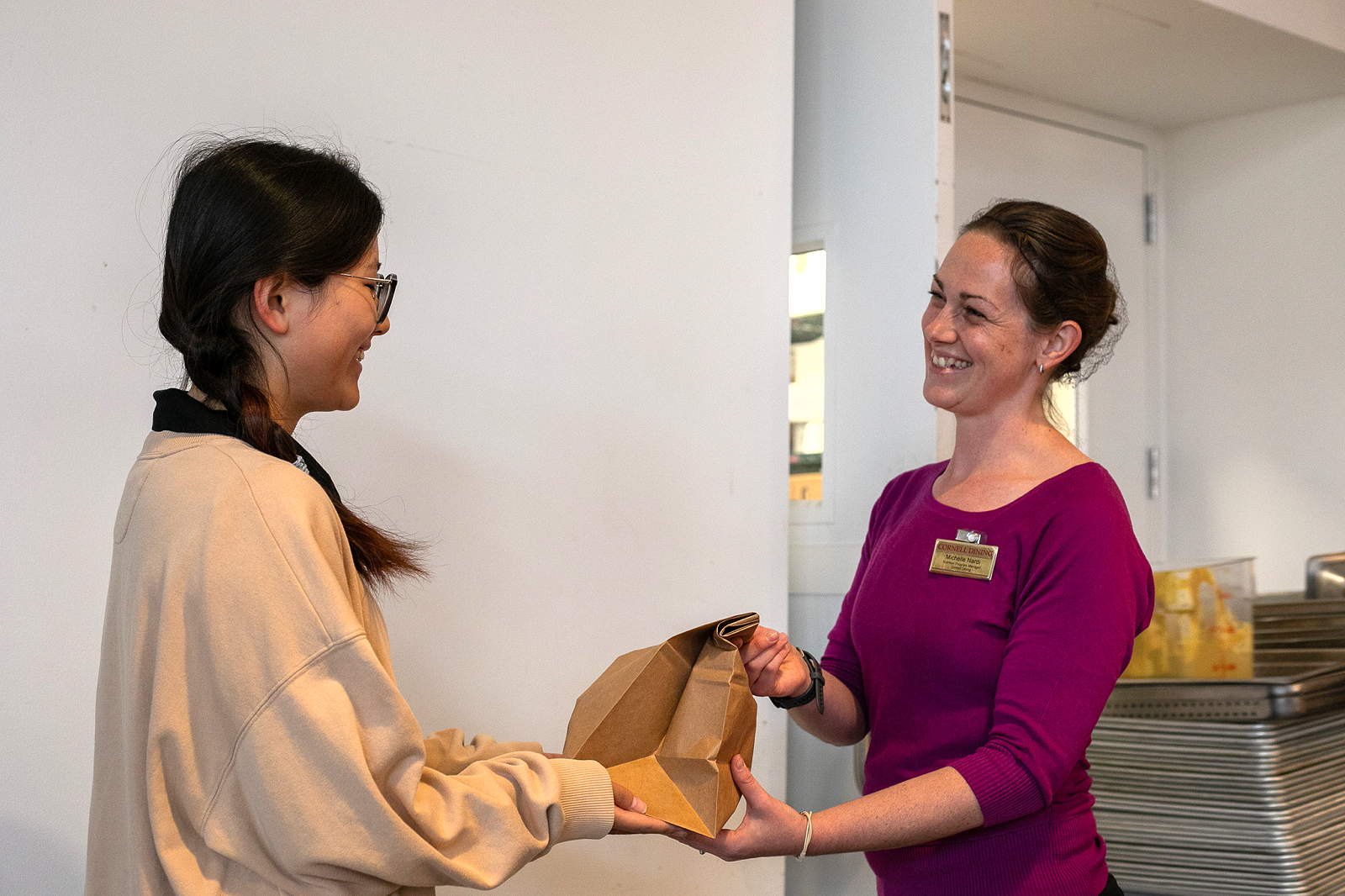 A smiling Dining staff member hands a bagged meal to a student