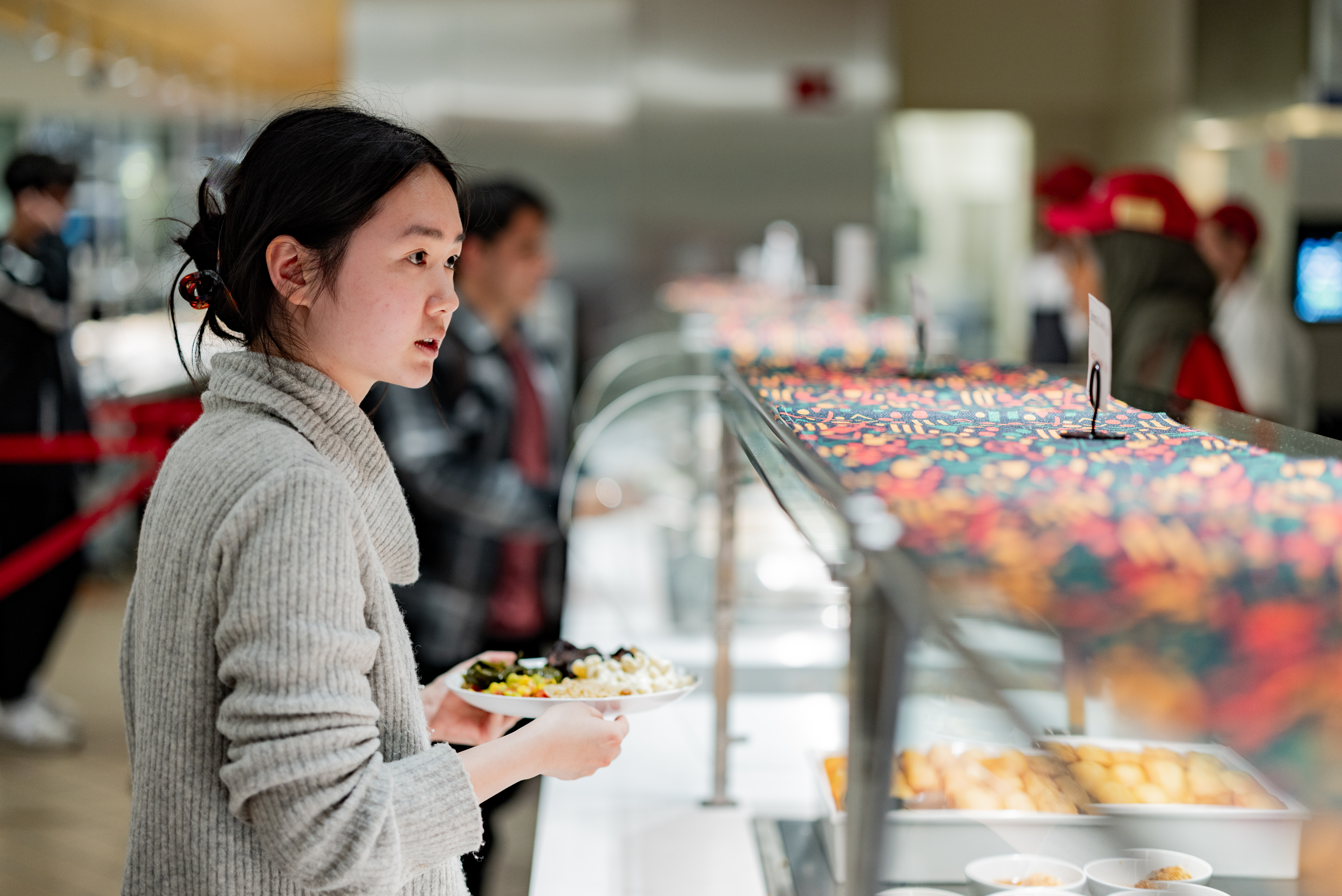 A young woman stands in front of a food serving station with a plate