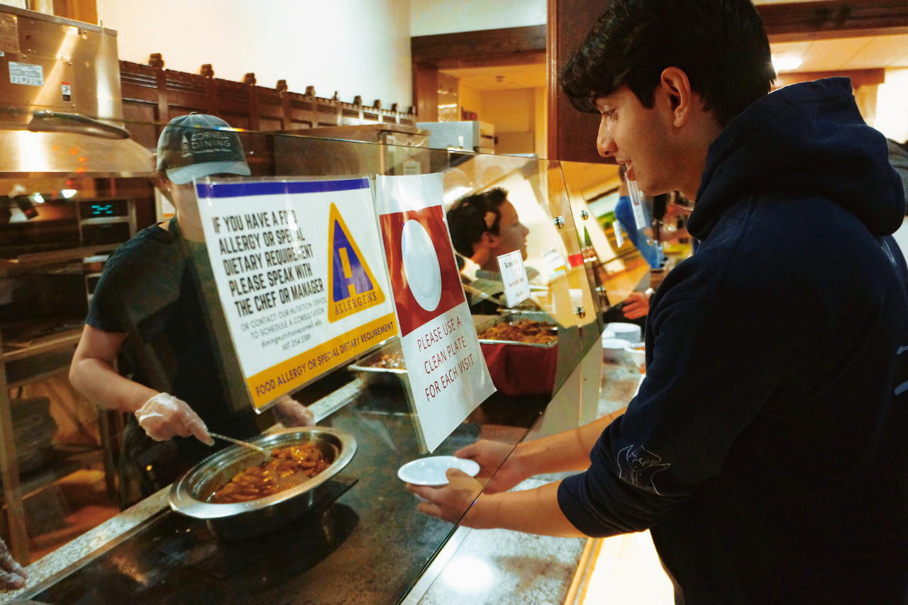 A staff member serves food to a student holding a plate