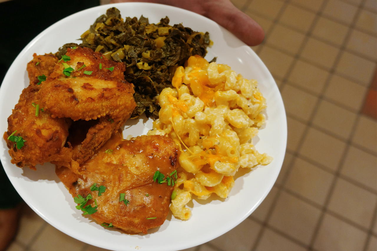 A hand holding a plate with fried chicken, greens, and mac and cheese