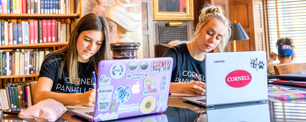 Two college women study in library on laptops