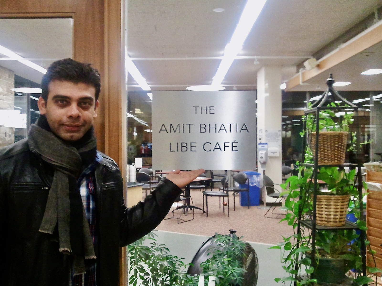 Amit Bhatia stands in front of the Libe Cafe door, holding his hand under the sign that says Amit Bhatia Libe Cafe