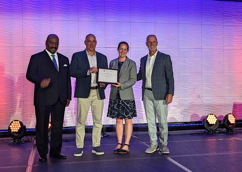 Four people stand on a stage, with one holding up an award
