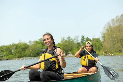 Two women paddling canoe in yellow life jackets
