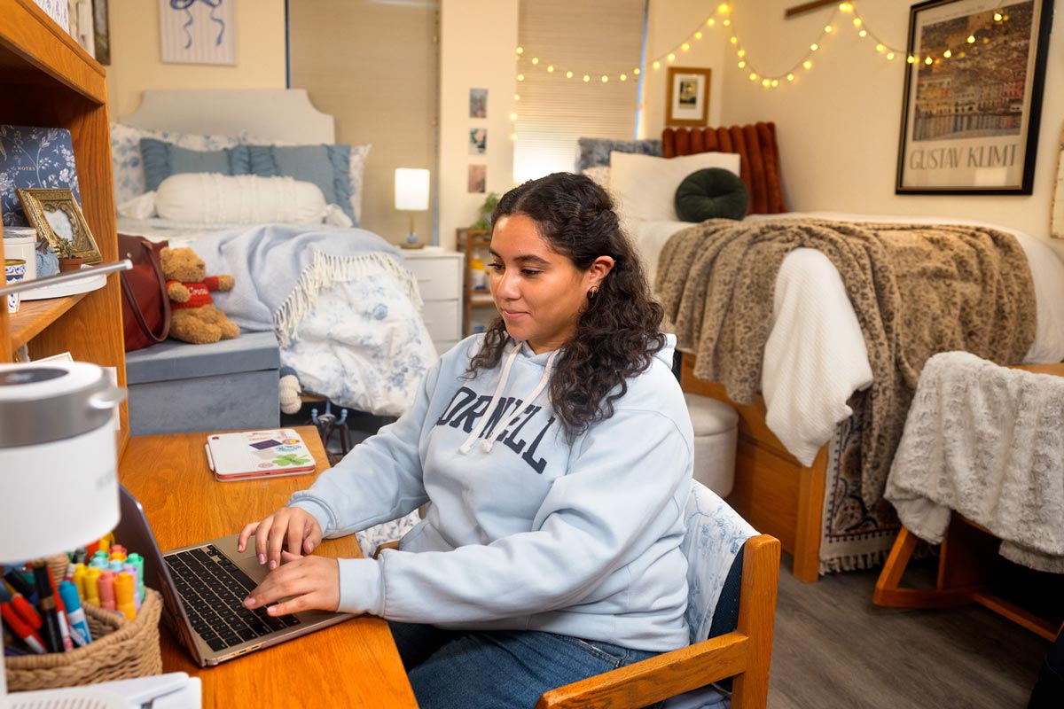 Femail student sitting at a desk in a residence hall and working on a laptop.