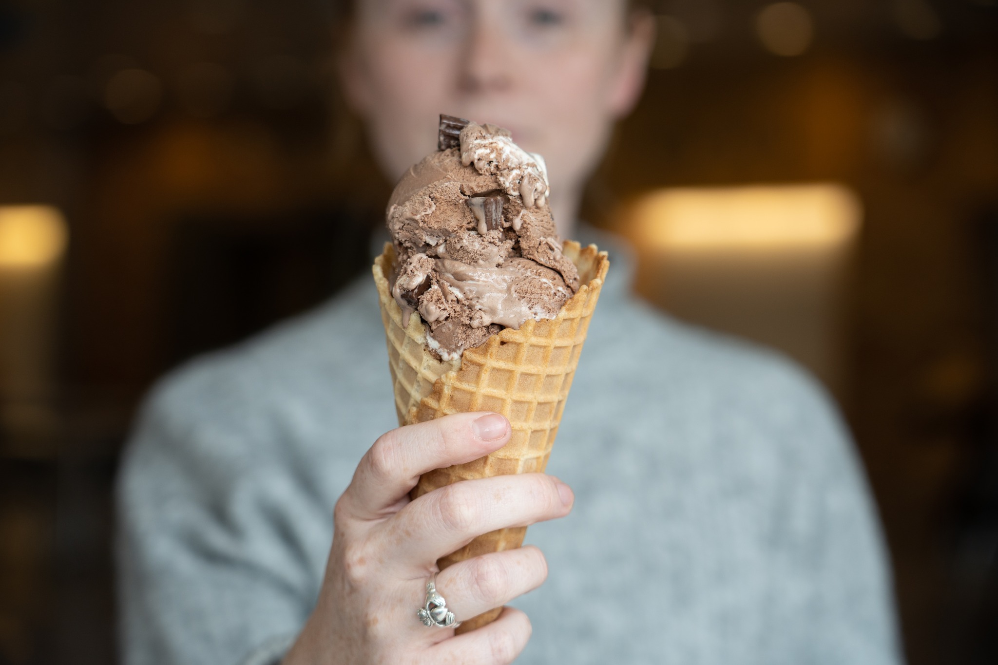 An ice cream cone held by a person who's visible in the background