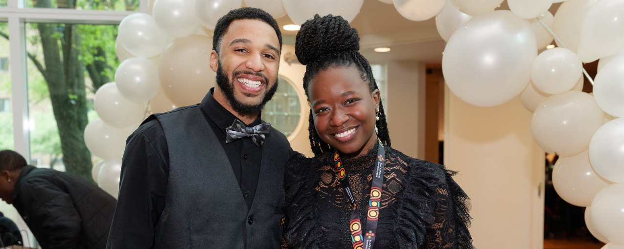 Two Black students pose under a balloon arch.