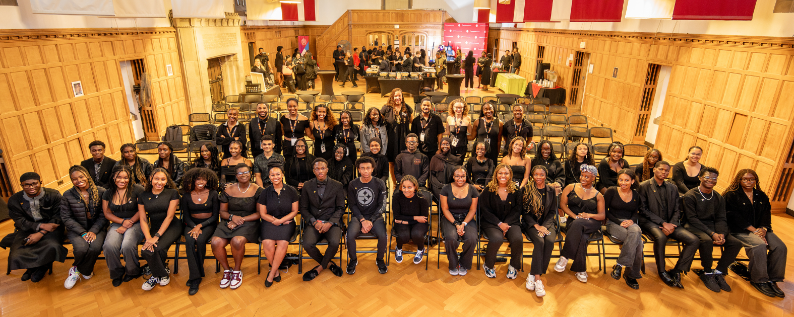 A large group of students pose during the first annual "Makandi New Student Welcome" event in Cornell's Memorial Room. They are all wearing black clothing.