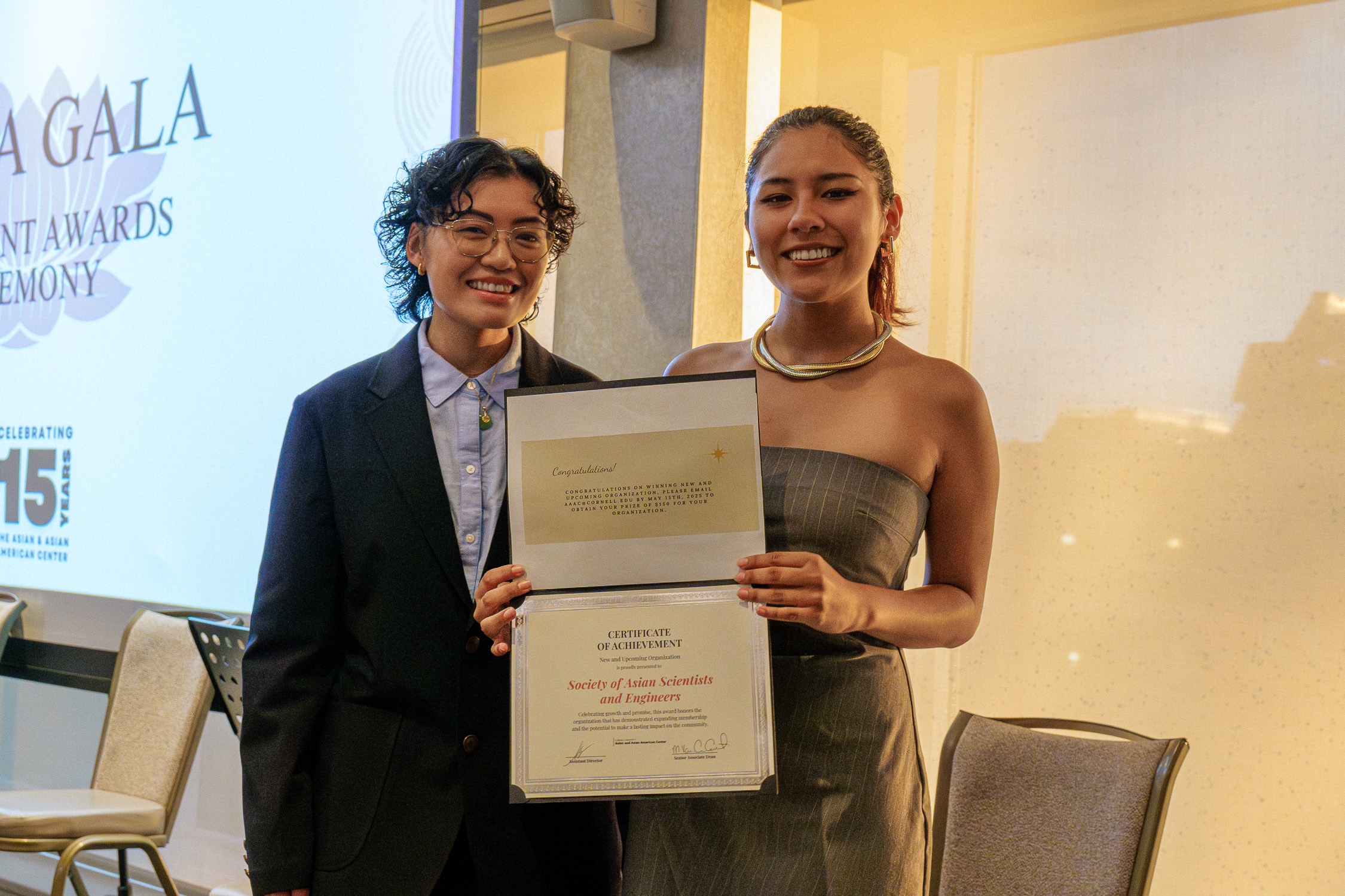 Award recipient holds a certificate and stands beside a smiling presenter during the APIDA Gala, where Cornell’s Society of Asian Scientists & Engineers was recognized as the New and Upcoming Student Organization of the Year.