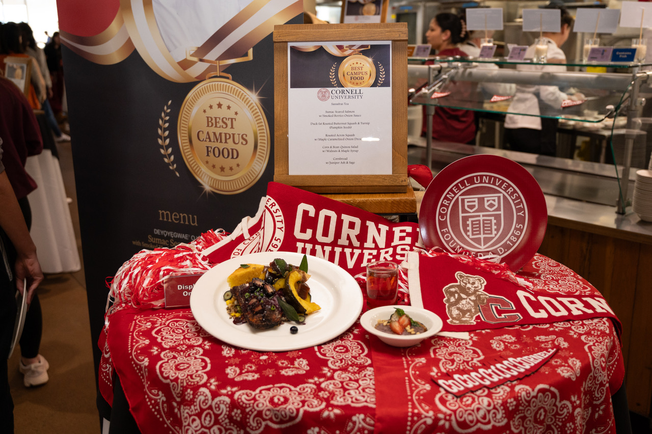 A table with red tablecloth and Cornell pennants, with plates of food and a Best Campus Food emblem