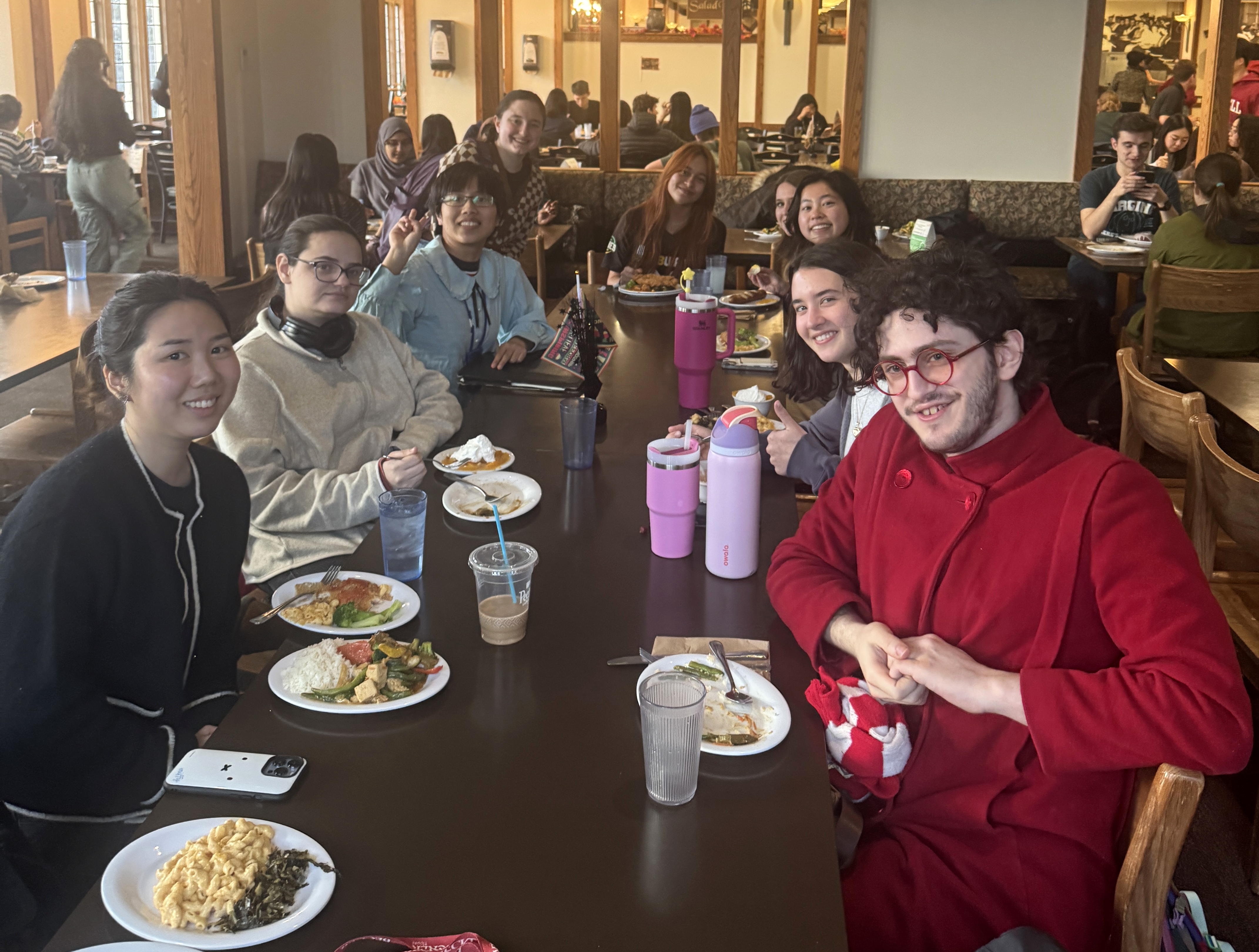 Several people around a table with plates of food smile and look toward us