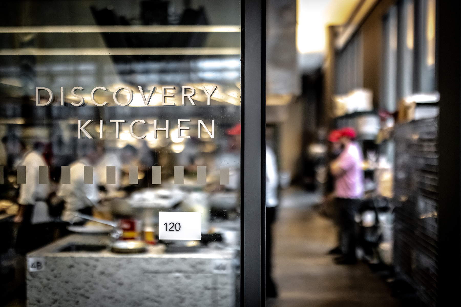 A view into a kitchen area past a glass wall with wording that says Discovery Kitchen