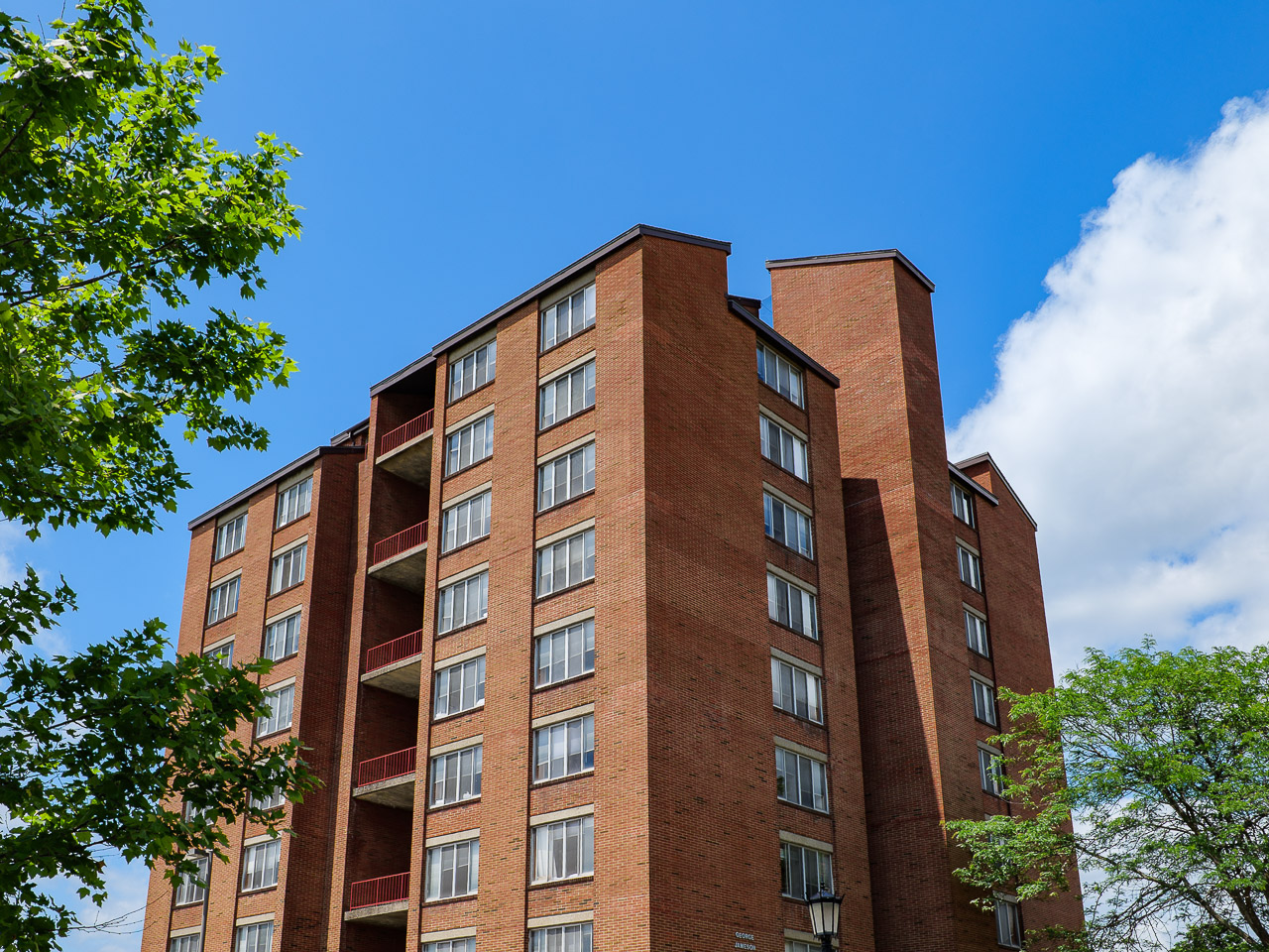 red brick high rise building with trees and clouds in the sky surrounding it.