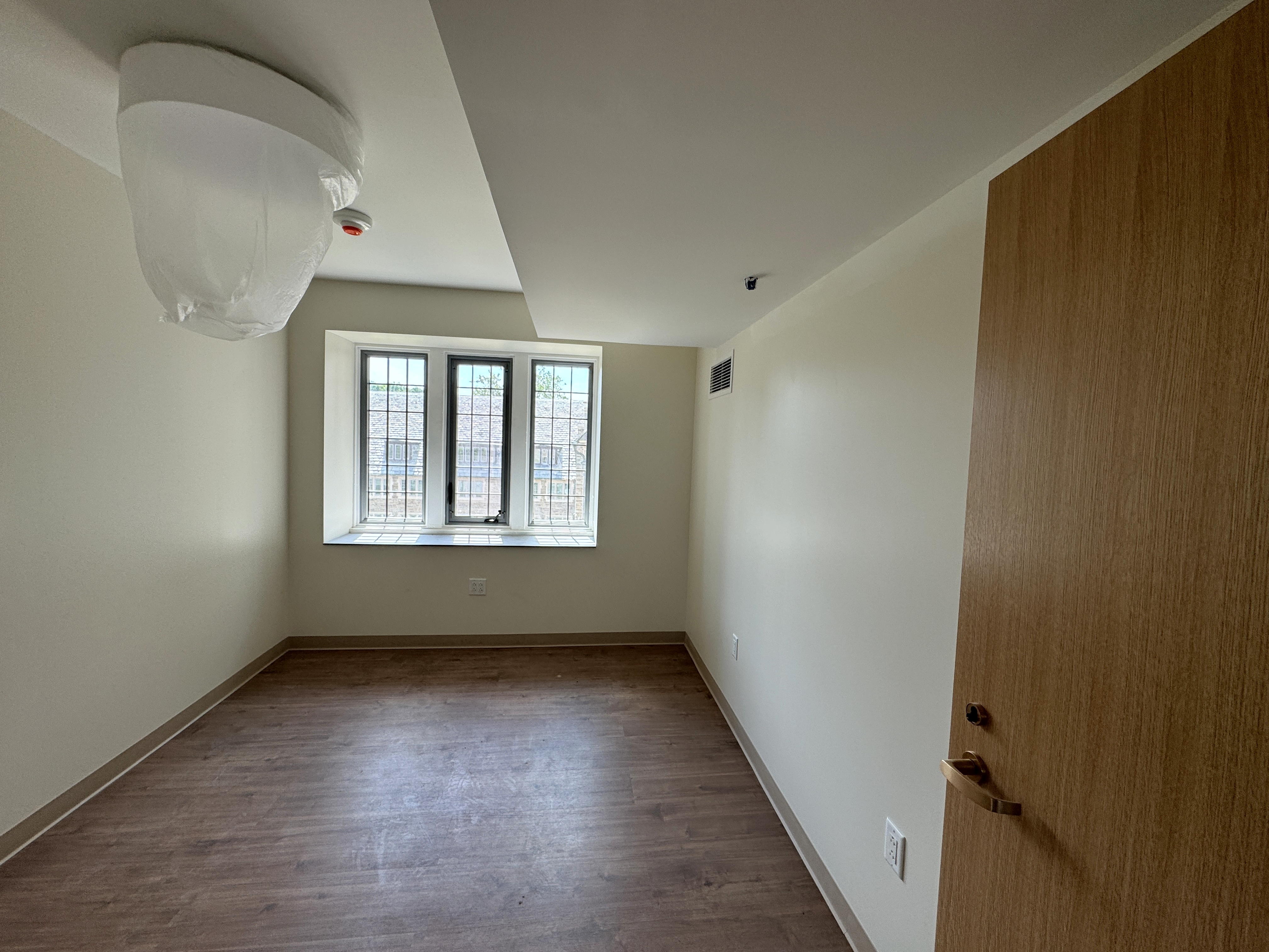 An empty residence hall room with the door open at right and windows at the far end