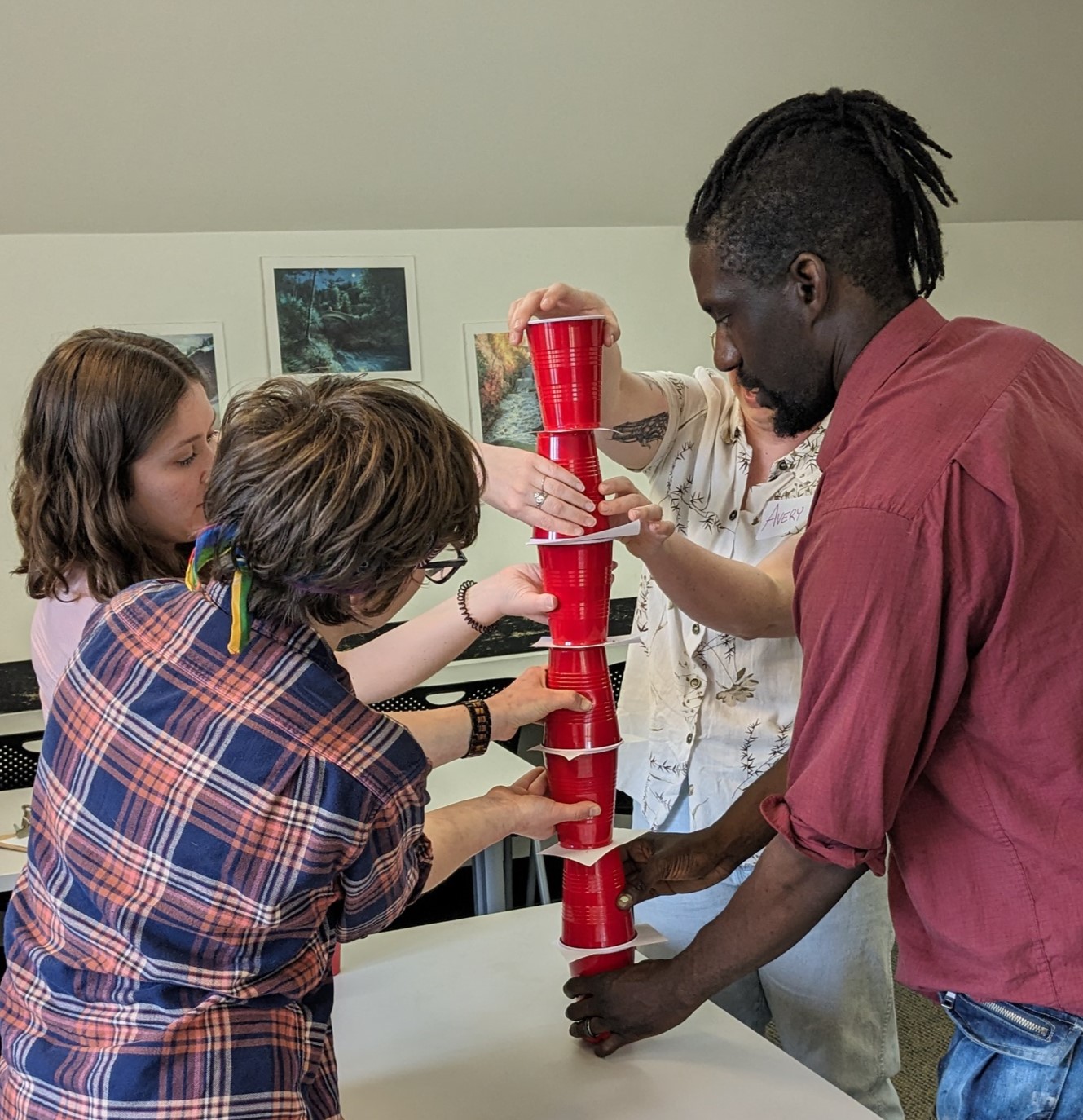 4 people supporting a stack of red plastic cups over a table