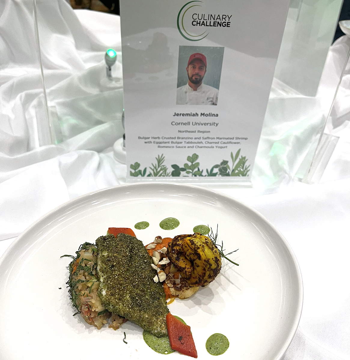 A plate of food with a placard identifying Jeremiah Molina of Cornell as the chef