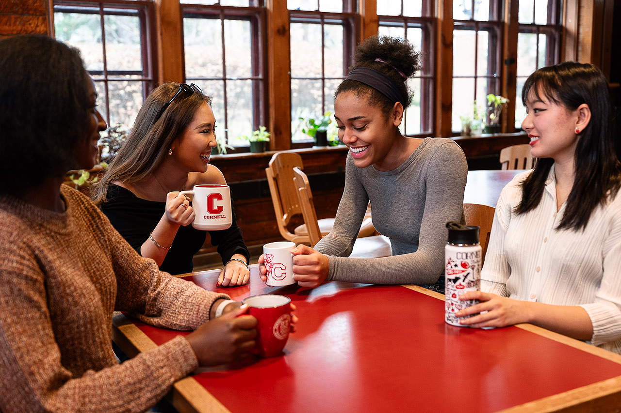 Smiling students sit around a table with coffee mugs