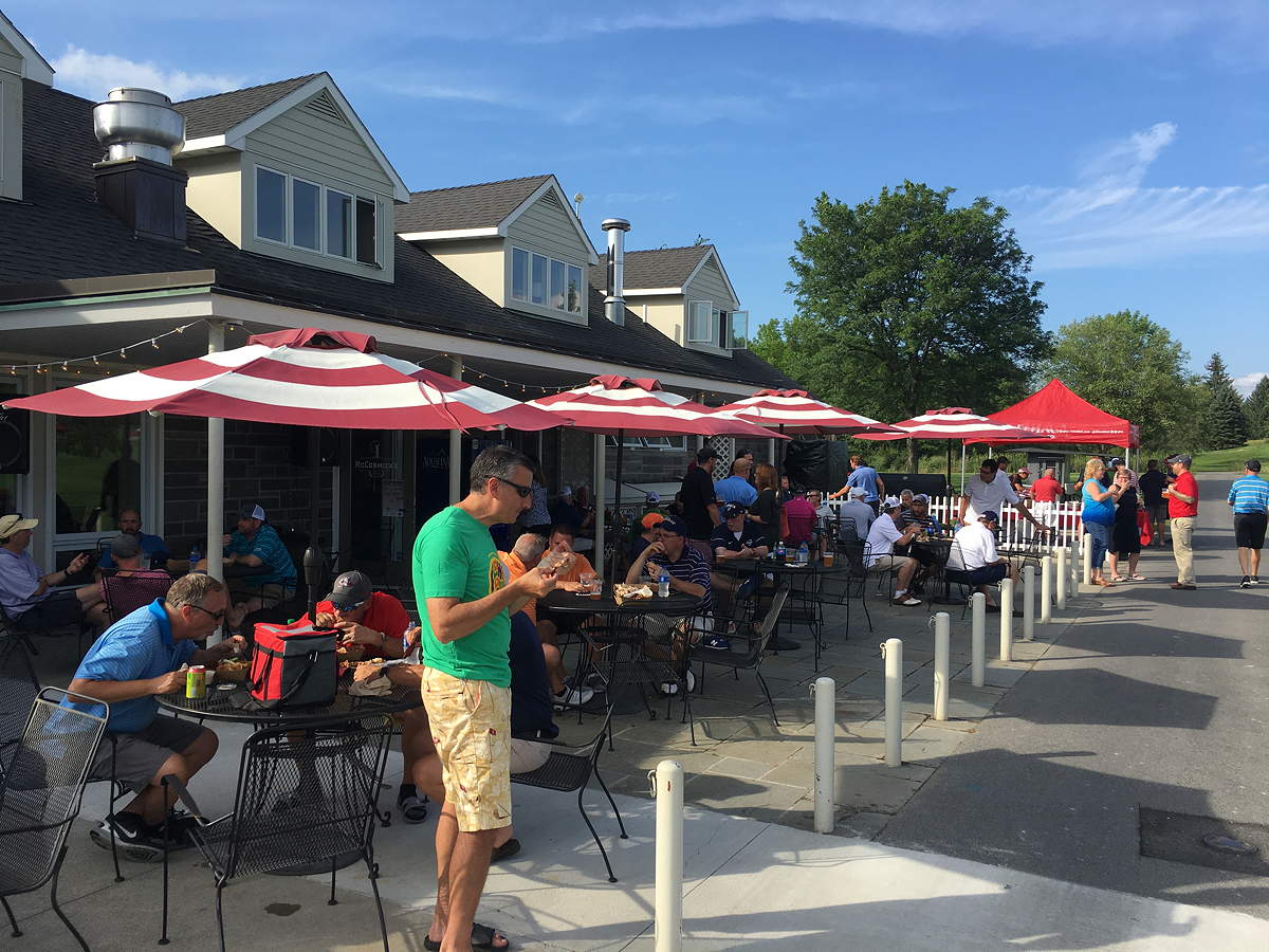 People seated at and standing around outdoor tables on a patio outside a building