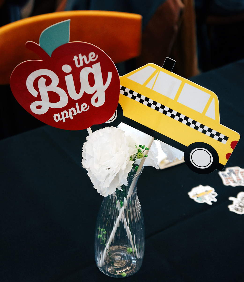 Table decorations sticking out of a vase include a flower, a yellow taxicab, and an apple with the words the Big Apple