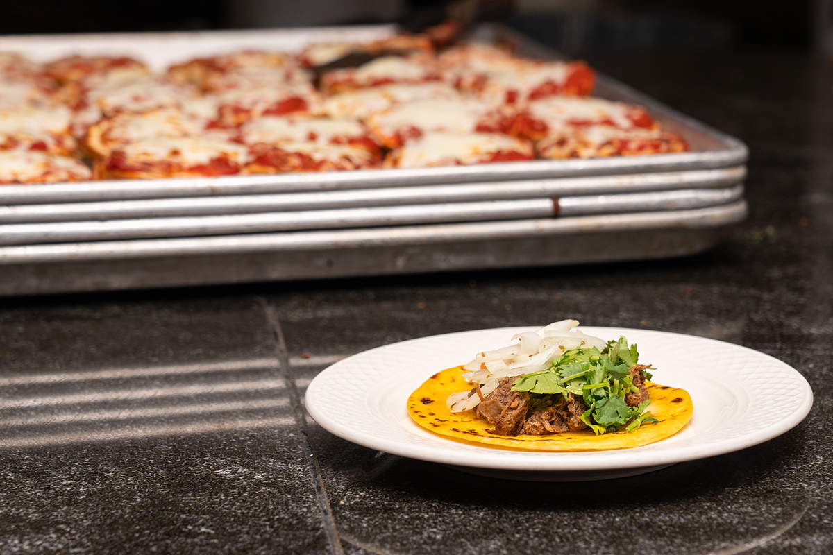 A plate with a taco, and a tray with portions of chicken parm in the background