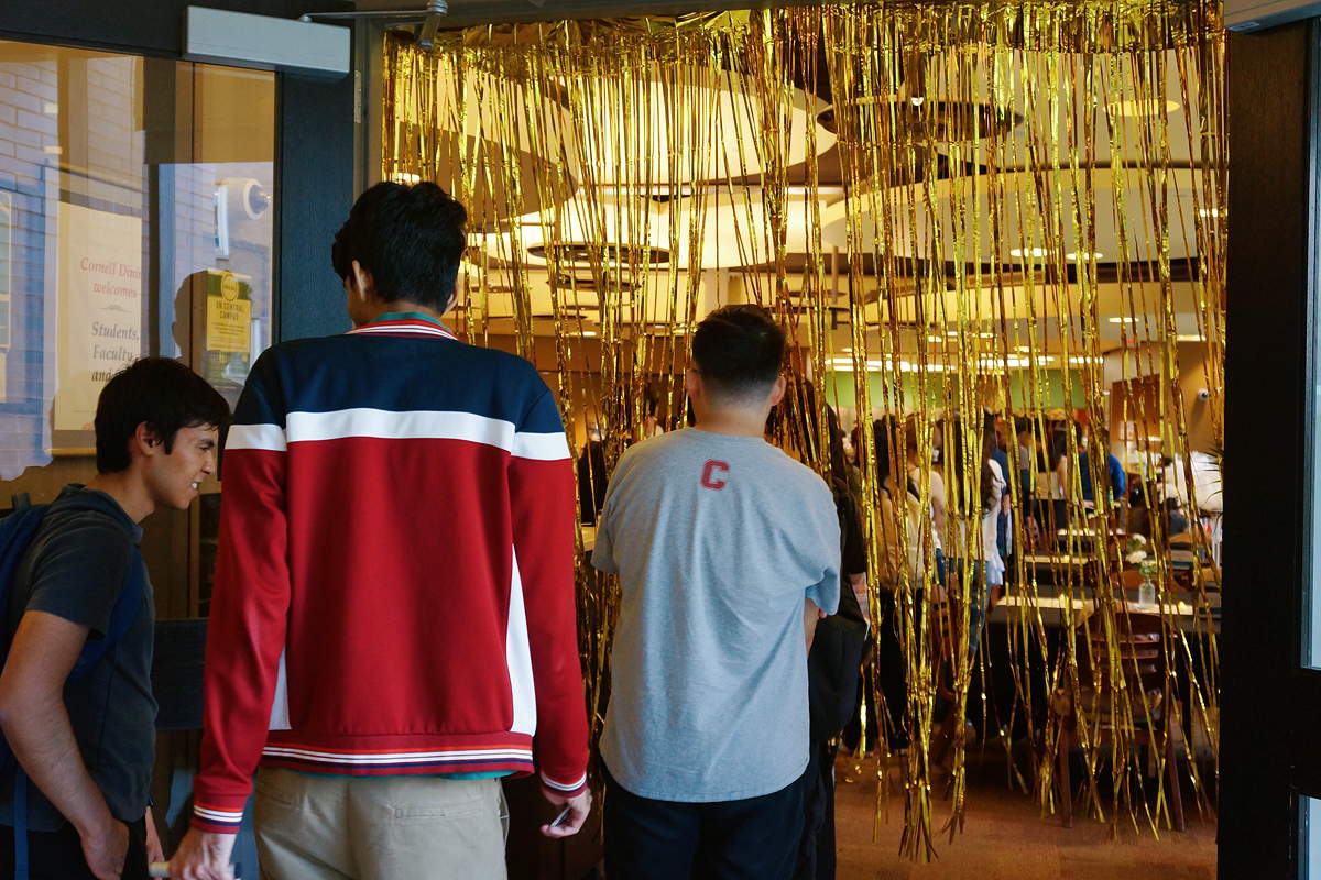 Three people approaching an entryway with gold streamers hanging down from the ceiling
