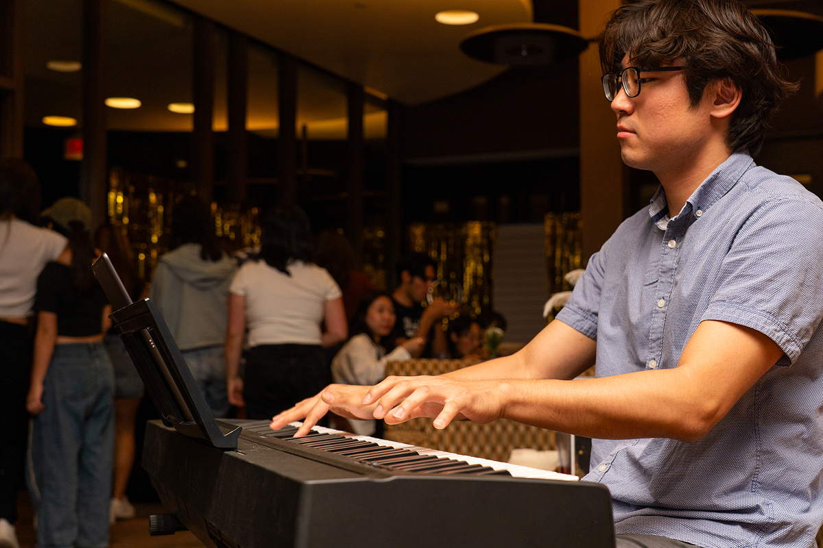 A person playing an electric keyboard in a dining room with people in the background