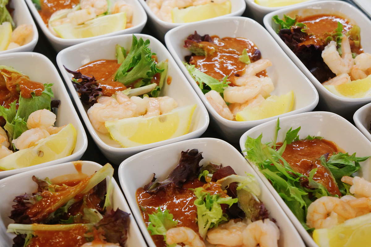 Small dishes each containing a few shrimp, a little cocktail sauce, a couple of lettuce leaves, and a lemon wedge