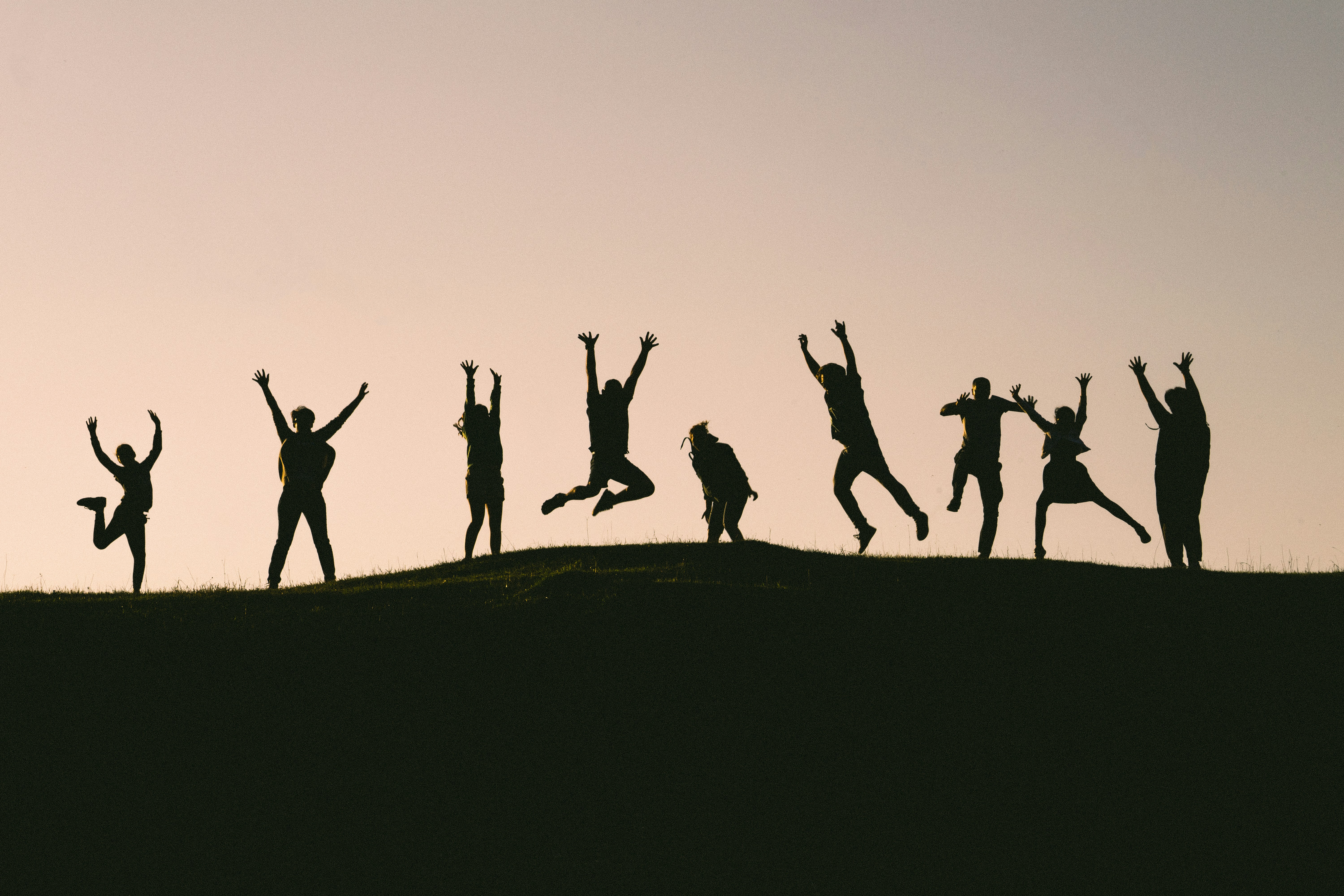 silhouette of students jumping up in the air on a hill