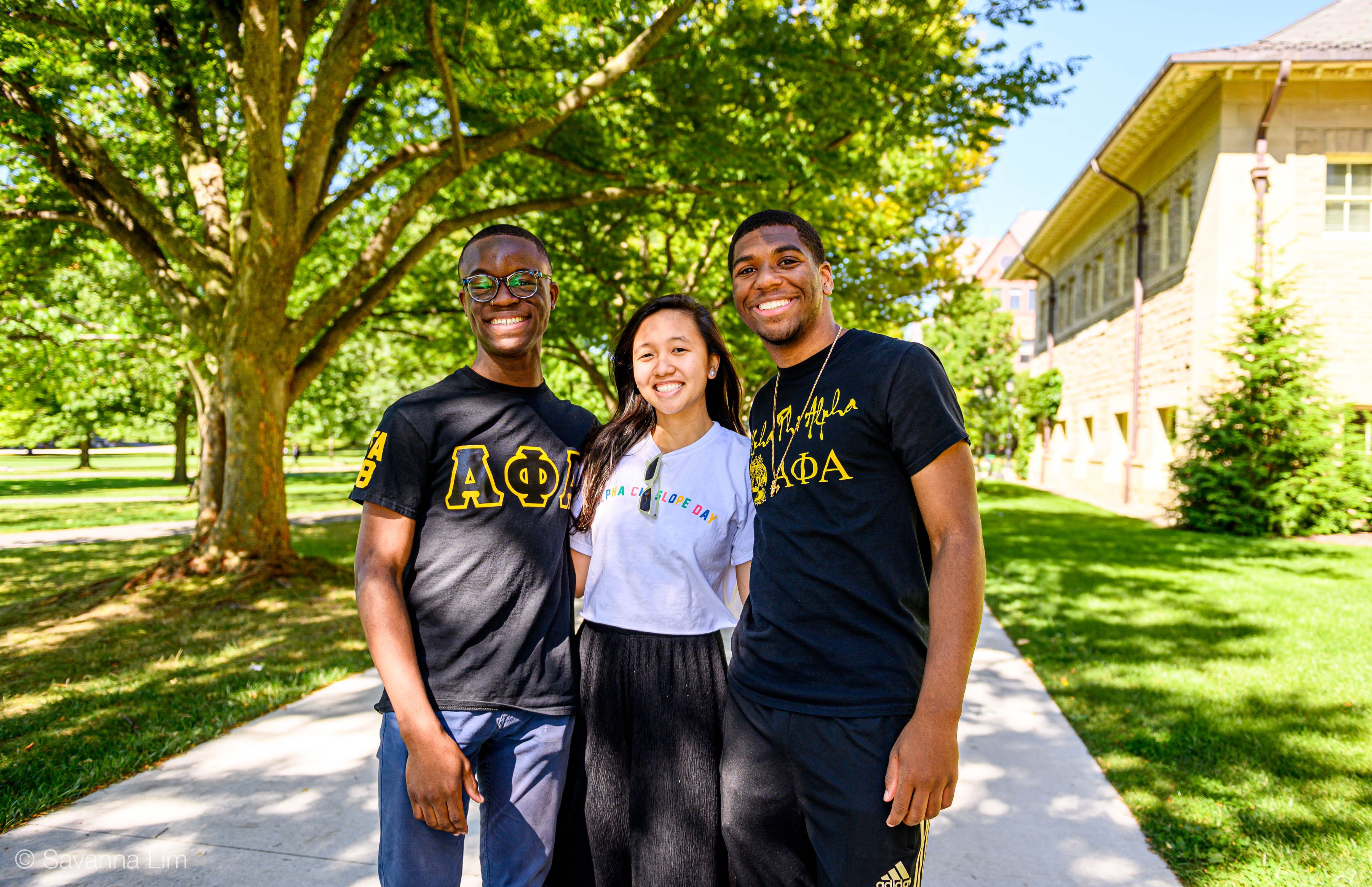 3 students standing togehter on a path smiling with their arms wrapped around eachother