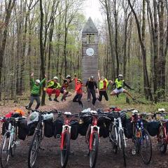 Bikes in a row on a path, near a wooden clock tower in the woods
