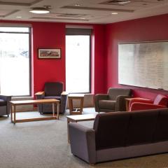 Lounge space in Court-Kay-Bauer Hall that has red walls, chairs, couches, tables, and a white board in it