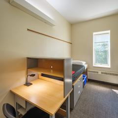 Single room with a twin bed, desk, chair, lamp, dresser, and window.