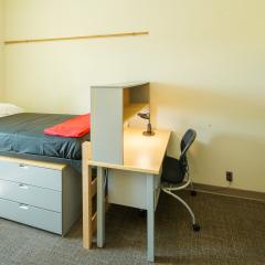 Single room with a twin bed, desk, chair, lamp, dresser, and window.