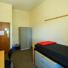 Single room with a twin bed, desk, chair, lamp, dresser, and window.