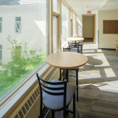 A large lounge in Cascadilla Hall with a large window, tables and chairs.