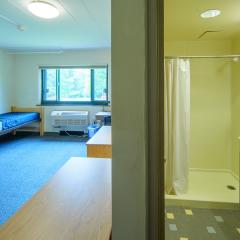 Double room with two twin beds, desks, chairs, lamps, dressers, a window and an attached full bathroom.