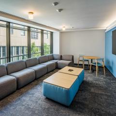 A lounge in Loving House with a table, chairs, a couch, coffee table, a tv and a large window. 