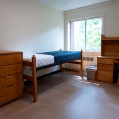 A bedroom with a twin bed, dressers, desk, and chair.