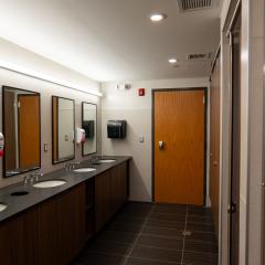 A communal bathroom with sinks, mirrors, counters, and stalls.